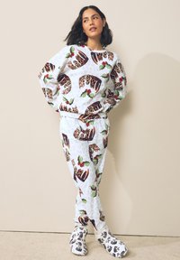 Witte loungebankset met een patroon van feestelijke desserts en hulstbladeren. Zachte stof, comfortabele pasvorm en bijpassende sloffen maken de look compleet.