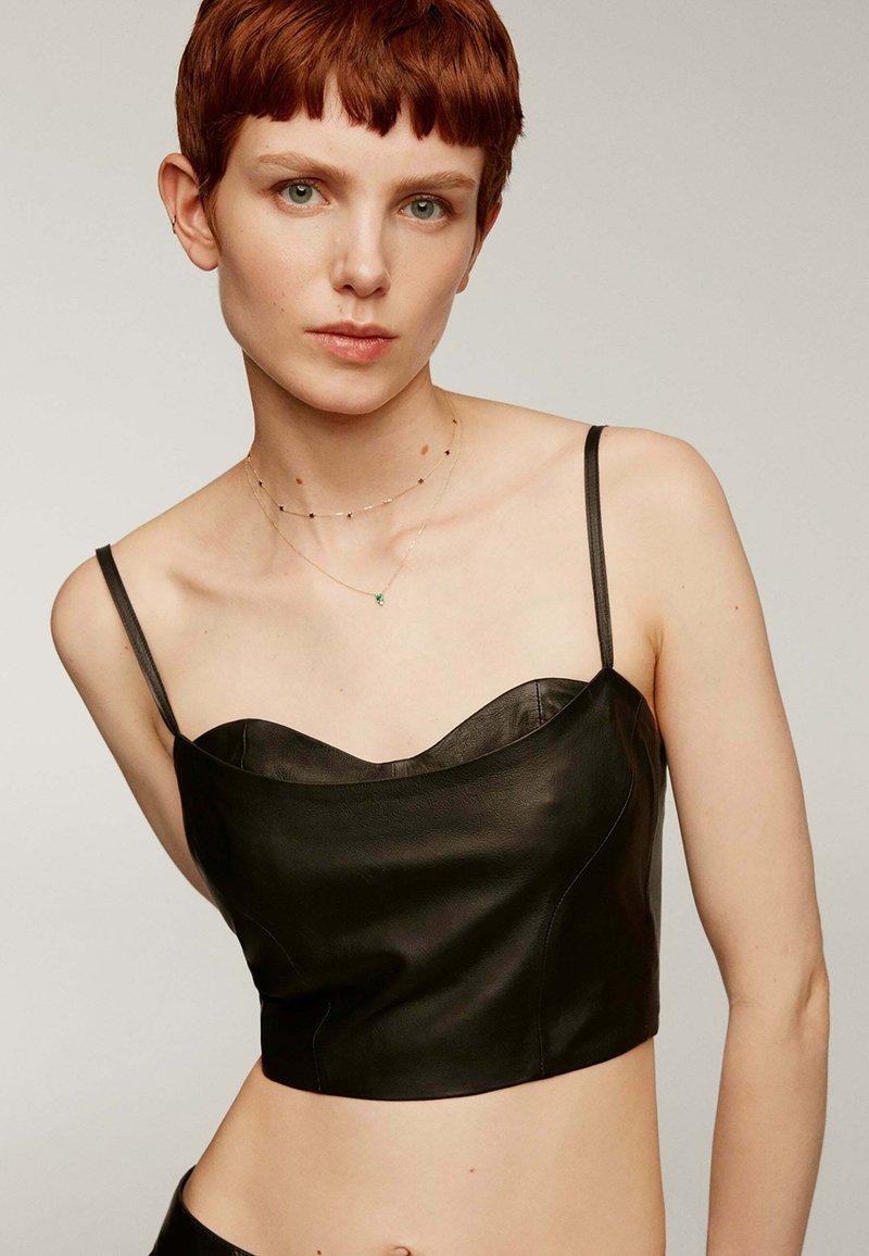 Top cortado de cuero negro con tirantes finos, que presenta un escote en forma de corazón y una textura suave. Sin patrones ni hardware notable presente.