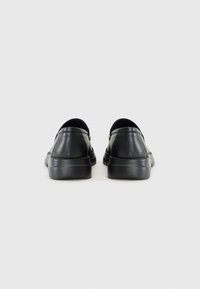 Black leather slip-on shoes with a rounded toe and flat rubber sole. Features a smooth finish and minimal stitching detail.