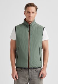 Green insulated vest with stand-up collar, front zip, orange accent, and two zippered side pockets. Made from lightweight, smooth material.
