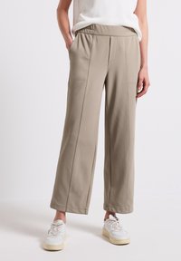 Beiga vida byxor i mjukt tyg med elastisk midja och sidofickor. Kombineras med vita sneakers som ger en avslappnad look.