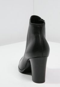 Bottine en cuir noir avec un talon carré, fermeture éclair sur le côté et tige lisse, photographiée sous un angle arrière trois quarts.