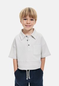 Ljusgrå kortärmad polo shirt med en strukturerad mönster, tre knappar och en bröstficka, som är kombinerad med marinblå shorts med dragsko.