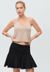 Top corto lavorato a maglia beige con spalline sottili, abbinato a una gonna nera svasata con dettagli arricciati e un bordo decorativo all'orlo.