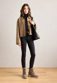 Brązowa skórzana kurtka cropped z czarnymi guzikami, czarny golf, czarne wąskie dżinsy oraz szare buty lace-up na grubej podeszwie. Czarna torba tote.