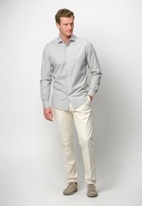Gestreiftes Button-Up-Hemd in Grau und Weiß, kombiniert mit cremefarbenen Hosen und beigen Sneakers. Der Stoff wirkt leicht und hat eine glatte Textur.