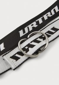 Verstelbare zwart-witte stoffen riem met een zilveren metalen D-ring gesp, voorzien van gedurfde tekstpatronen die in de banden zijn geweven.