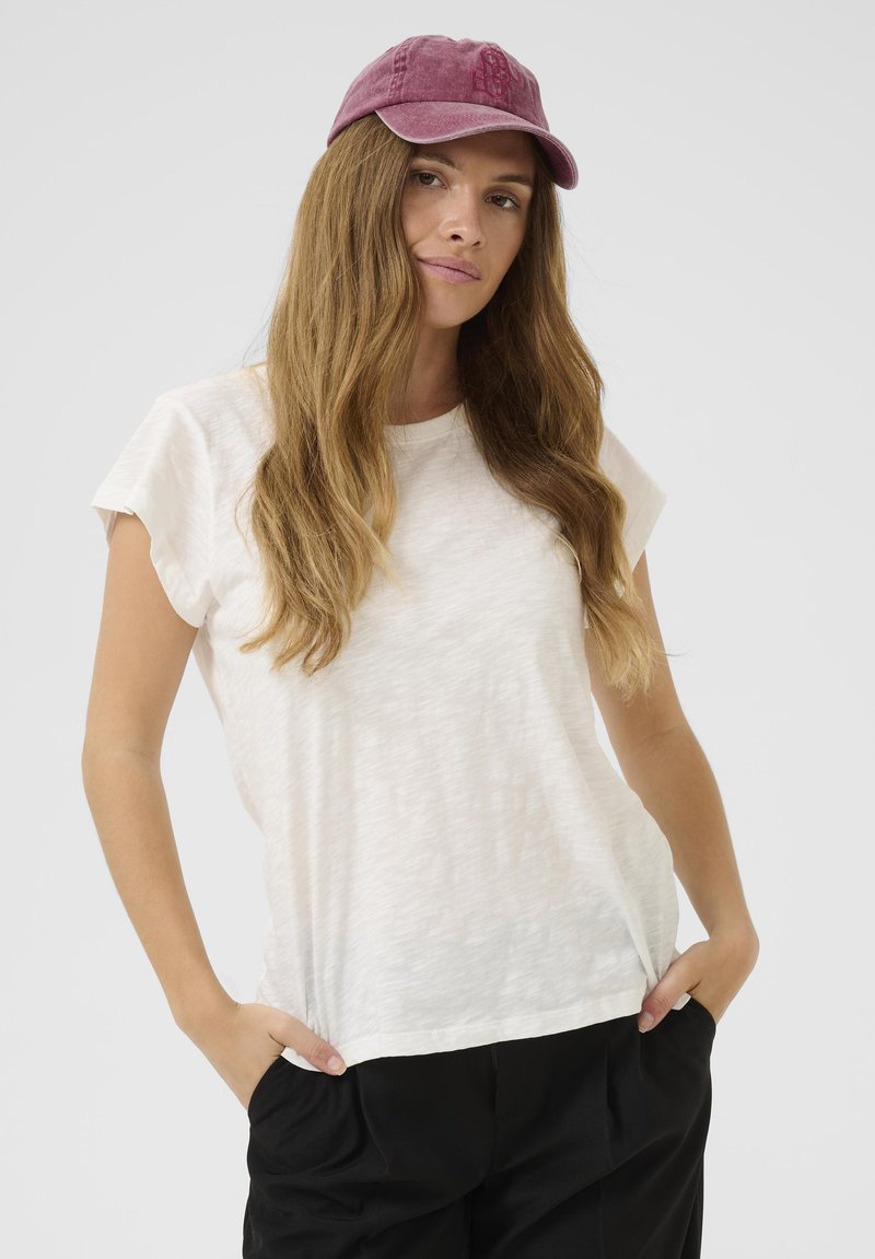 Camiseta blanca de manga corta con un acabado suave y texturizado, combinada con una gorra burdeos. La camiseta tiene un corte relajado y un cuello redondo.