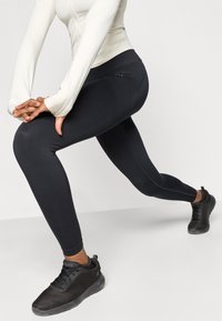 Μαύρα αθλητικά κολάν με απαλή υφή και εφαρμοστό σχέδιο. Συνδυασμένα με σκούρα αθλητικά παπούτσια από πλέγμα που διαθέτουν υφασμάτινες λεπτομέρειες και κορδόνια.