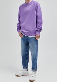 Sweat-shirt violet à col rond, manches longues et poignets côtelés, associé à un jean bleu clair fuselé et des baskets blanches.