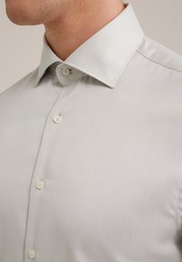 Világosszürke, gombos ing texturált anyagból. Klasszikus gallérral, standard gombokkal és szőtt mintával a további részletekért.