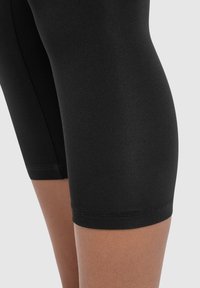 Leggings neri fino al ginocchio realizzati in un tessuto liscio e elastico. Presentano un design aderente con orlo pulito e senza motivi o dettagli visibili.