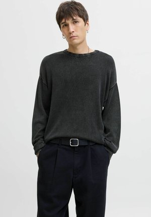 Jersey gris de punto con un corte relajado, cuello de canalé y mangas largas, usado sobre pantalones oscuros con plisados y un cinturón negro.