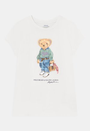 Wit T-shirt met illustratie van een teddybeer die een groene trui, blauwe spijkerbroek, sneakers draagt en een handtas met een roze lint vasthoudt.