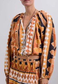 Blusa corta de manga larga y falda a juego en patrones naranja, negro y blanco. Tela suave con cintura elástica y detalle de cordón.