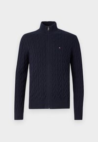 Mørkeblå strikket cardigan med høy krage og glidelås foran. Har et strukturert kabelmønster og ribbestrikkede mansjetter og kant. Liten logoakcent.