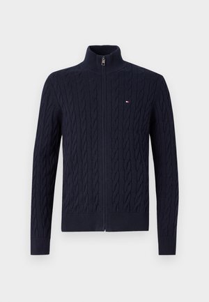 Marineblå strikket cardigan med høj krave og lynlåslukning fortil. Har et struktureret kabelmønster samt ribstrikkede manchetter og kant. Lille logo-accent.