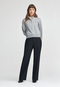 Maglione grigio a zip con orlo a coste, abbinato a pantaloni neri a vita alta e a gamba larga. L'outfit presenta un colletto classico sotto il maglione.