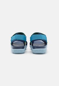 Blå och grön sandal med justerbara remmar, texturad sula och logotyp på häl, med en lättviktig och flexibel design.