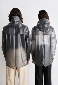 Deux personnes portent des imperméables contrastés, l'un gris et l'autre avec un dégradé de gris à blanc. Tous deux ont des capuchons et une finition lisse et brillante.