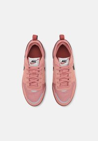 Rožiniai Nike sportbačiai, pagaminti iš tinklelio ir zomšos medžiagų, apvaliu pirštu, su raištelių uždarymu ir juodu swoosh logotipu šone.