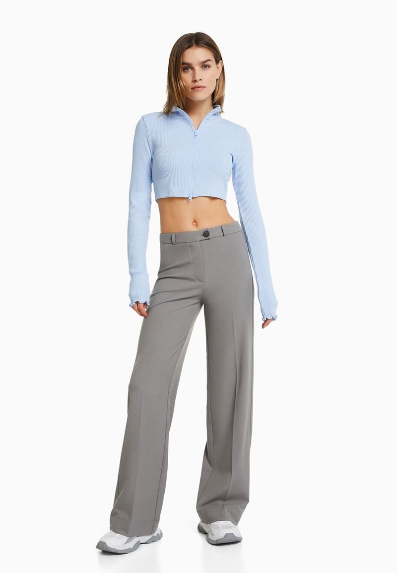 Un crop top côtelé bleu clair avec une fermeture éclair à l'avant, associé à un pantalon large gris taille haute et des chaussures de sport blanches.