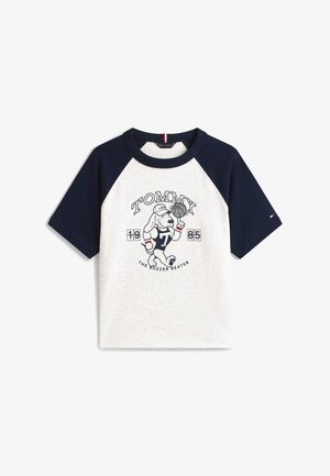 Λευκό και ναυτικό μπλουζάκι ράγκλαν με καρτούν σκύλο που παίζει μπάσκετ, με κείμενο "TOMMY", "1985" και "The Buzzer Beater" στο μπροστινό μέρος.