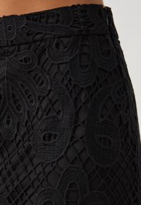 Närbild av svart kjol med intrikata spetsbroderier som visar blommiga och geometriska mönster på tyget.