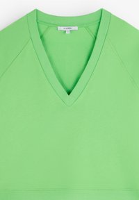 Pulover verde cu decolteu în V, cu detalii cu nervuri la guler și la tiv. Textură netedă, cu mâneci raglan și croi lejer. Mărimea S.