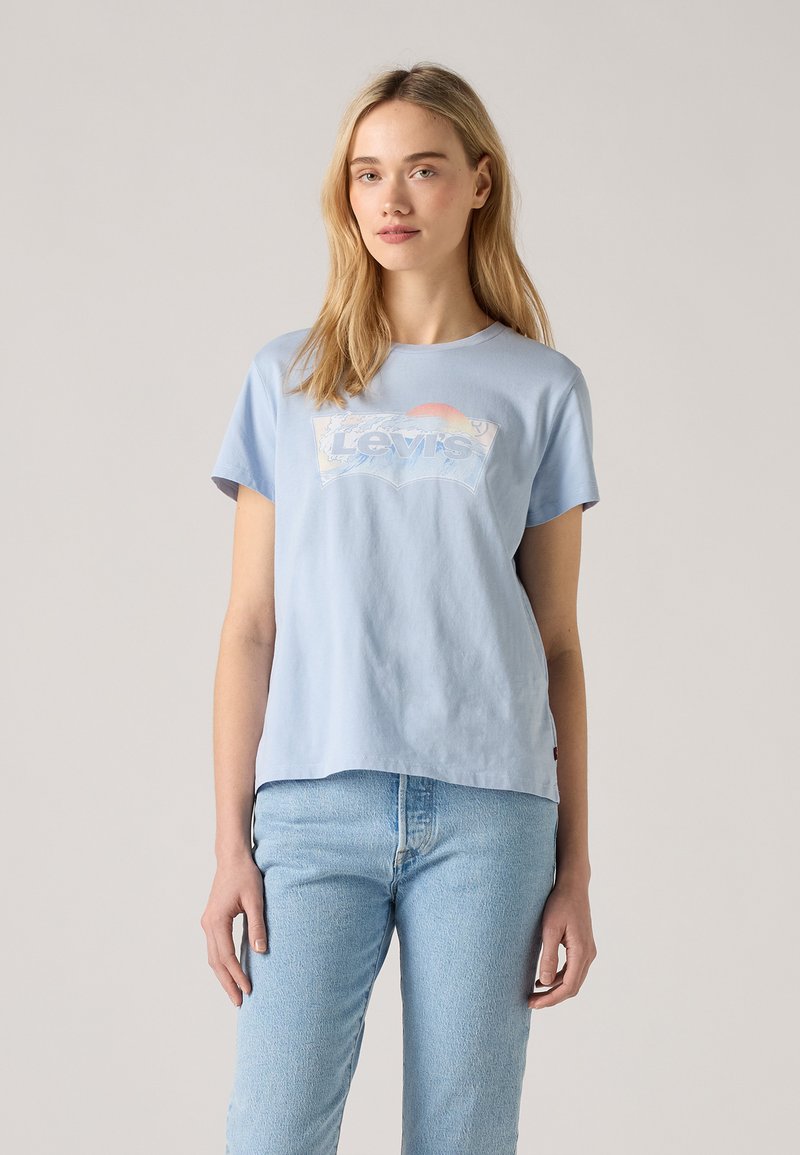 Šviesiai mėlynas medvilninis T-marškinėlis su dideliu baltu Levi's logotipu ir saulėlydžio dizainu, trumpomis rankovėmis ir laisvu siluetu.