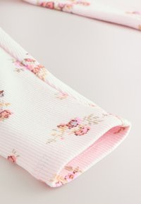 Pink ribbed fabric with a floral pattern, featuring small roses and leaves in pastel colors. Soft texture and rolled hem detail.
