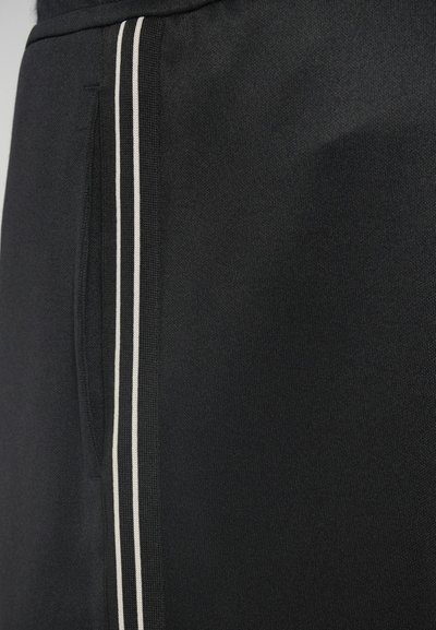 Čierne športové šortky vyrobené z textúrovanej látky, s bočnou vreckom a dvoma kontrastnými bielymi vertikálnymi pruhmi pozdĺž švu.