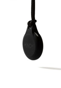 Schwarzes, rundes Etikett aus Gummi mit embossed "KNOK"-Logo. Hängt an einem schwarzen Cord und hebt die glatte Textur und das minimalistische Design hervor.