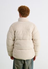 Faux fur cream puffer jacket with a high collar, textured surface, and wide sleeves, paired with light blue baggy jeans.