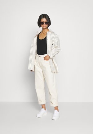 Randig oversized skjorta i vitt och svart, svart linne, krämfärgade högmidjade jeans och vita sneakers. Mörka solglasögon fulländar looken.