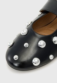 Μαύρο δερμάτινο παπούτσι με στρογγυλή μύτη, διακοσμητικές ασημένιες μεταλλικές σ studs διαφόρων μεγεθών και κομμένη πλευρική σχεδίαση με επίπεδη σόλα.
