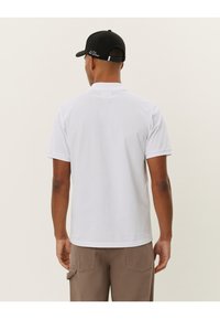Chemise polo blanche à manches courtes, col côtelé et ourlet droit. Le dos présente un design uni. Portée avec un pantalon cargo beige et une casquette noire.