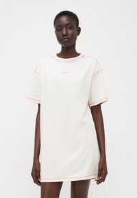 Abito corto bianco con scollo rotondo e cuciture rosa. Presenta un piccolo logo "HUGO" centrato sul petto. Materiale in cotone, vestibilità rilassata.