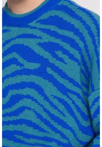 Stickad tröja med ett blått och teal zebramönster. Mjuk textur med rund halsringning och ribbade ärmslut för en tät passform.