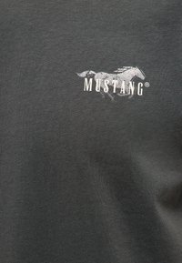 Tissu gris foncé avec un graphisme blanc représentant un cheval au galop et le texte « MUSTANG » imprimé en haut à gauche.