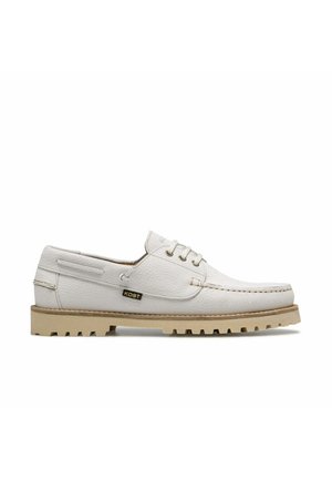 Chaussure bateau en cuir blanc avec semelle crantée beige, trois œillets pour lacets, et petite étiquette noire « KOST » sur le côté.