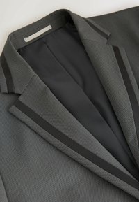 Blazer gris con una tela texturizada, ribete satinado negro a lo largo de la solapa y el cuello, y un forro interior suave.