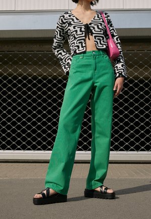 Pull en noir et blanc, découpé, avec un motif abstrait, associé à un jean large taille haute vert fluo et des sandales à plateforme noires.