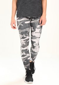 Szare legginsy w kamuflażu z teksturowanym wzorem, dopasowany krój i czarne sneakersy. Prosty szary top częściowo zakrywający legginsy.