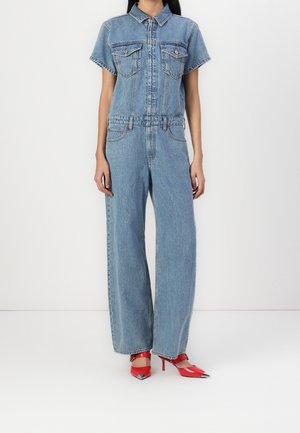 Blå denim jumpsuit med korte ærmer, forlommer og belte omkring taljen. Sættes sammen med røde spidse hæle.