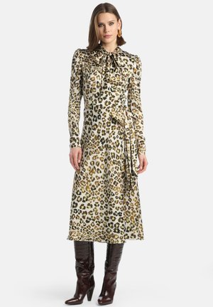 Luipaardprint jurk met een hoge kraag, lange mouwen en een strikceintuur. Heeft een vloeiende silhouet en is gecombineerd met bruine laarzen met krokodillenprint.