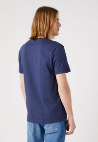 T-shirt in cotone blu navy con maniche corte, collo tondo e una texture liscia; indossato con jeans in denim blu chiaro, visto di spalle.