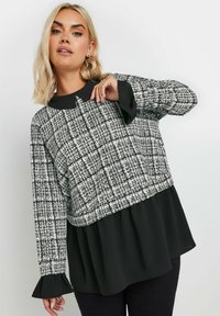 Top a strisce in bianco e nero con colletto, maniche lunghe e polsini arricciati, design a strati con una sezione inferiore nera uniforme.