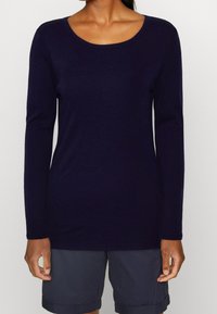 Mörk marinblå långärmad topp i ett mjukt, slätt tyg. Har en rund halsringning och en figurnära silhuett. Bärs tillsammans med gråa shorts.