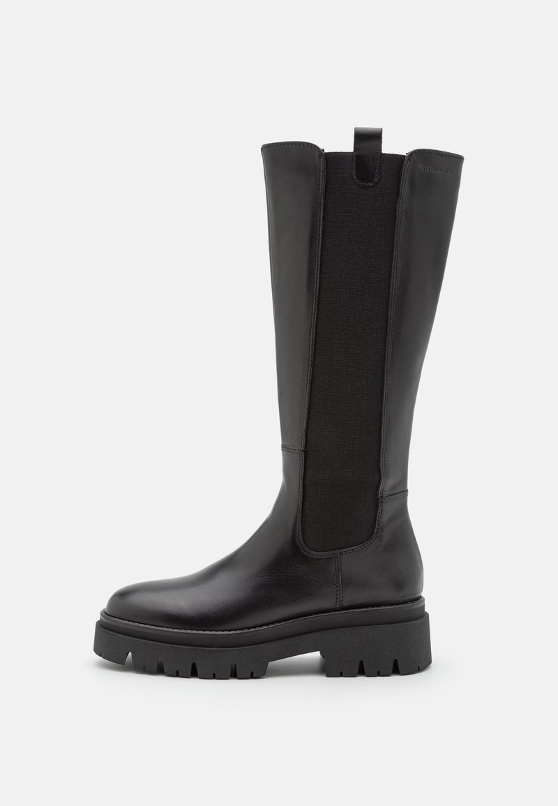 Botte en cuir noire hauteur genou avec semelle à crampons épaisse et panneau latéral élastique sur fond blanc.